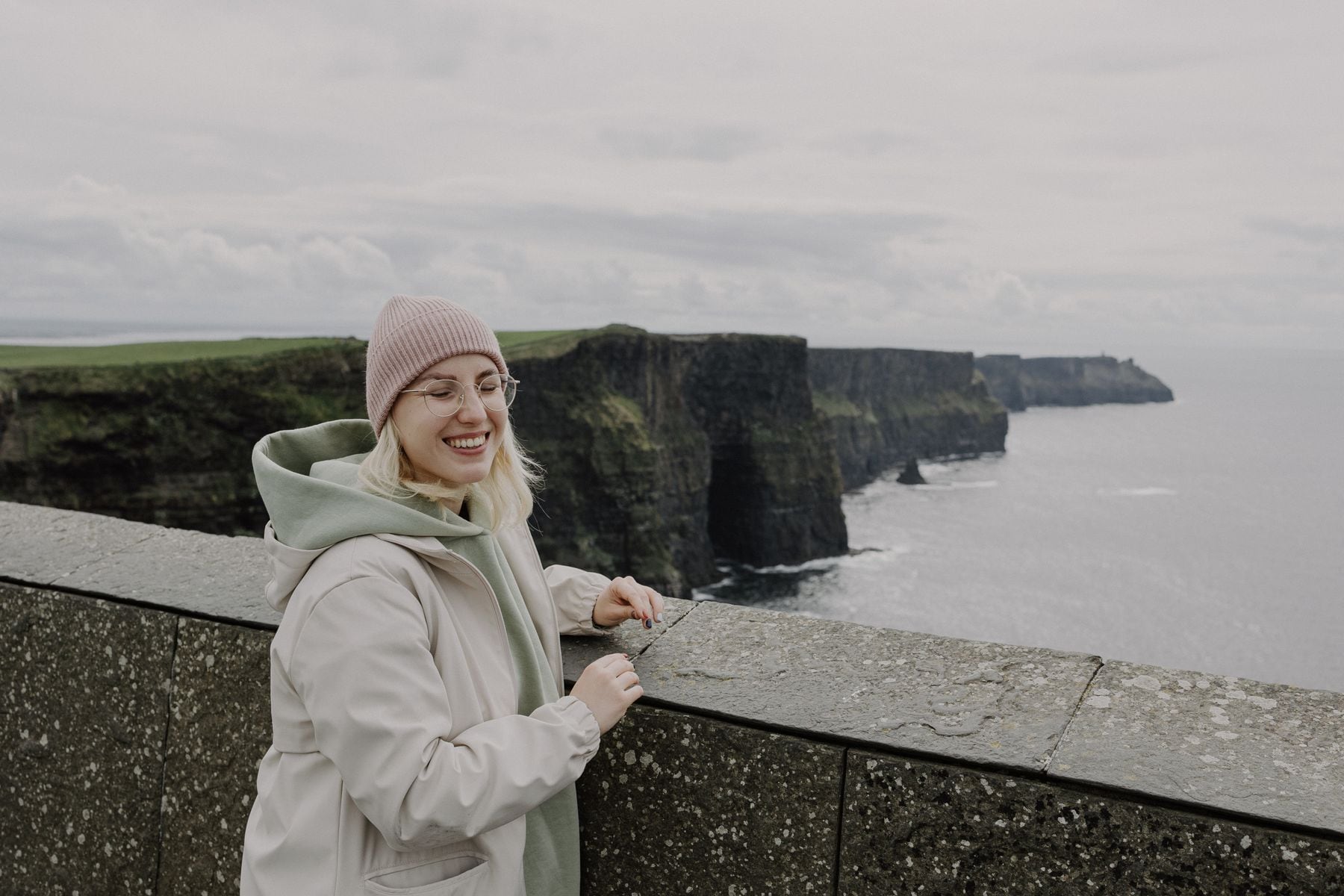 A smiling woman taking a pause beside the Cliffs of Moher in Ireland